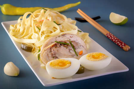 Noodles with pieces of meat and eggs in a white plate and dim sum with various traditional mushroom, soy and vegetable appetizers with chopsticks on a blue table. Asian food conceptの写真素材