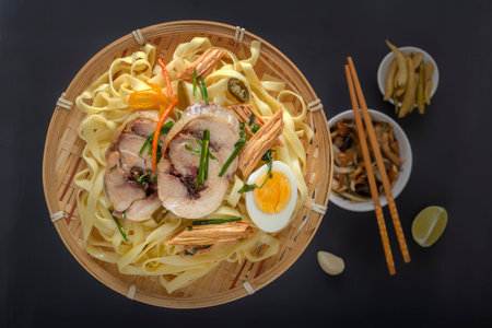 Noodles with pieces of meat and an egg in a bamboo plate on a dark table. Asian food concept. View...