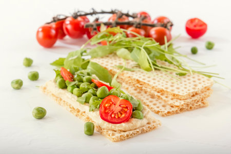 Crispy low calorie wheat crackers with green peas, arugula, microgreens and tomatoes on a white...