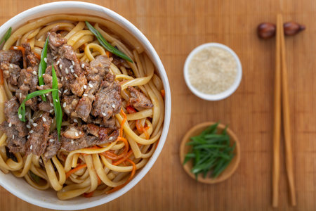Noodles with meat, pepper, herbs and sesame seeds in a paper disposable plate on the background of a...