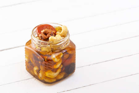 Mixture of walnuts, cashews, raisins, dried apricots and prunes with honey in a glass jar on a white wooden table. Copy spaceの写真素材