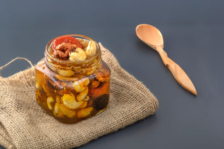 Mixture of walnuts, cashews, raisins, dried apricots and prunes with honey in a glass jar and a...