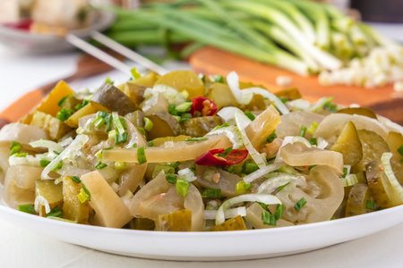 Slicing fermented green tomatoes and cucumbers with pickled garlic onions in a white plate on a light table. Close-upの写真素材