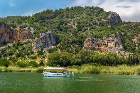 Dalyan, Turkey - May 9, 2022. Tourist pleasure boat on the river next to the rocks in which the Lycian tombs are locatedのeditorial素材