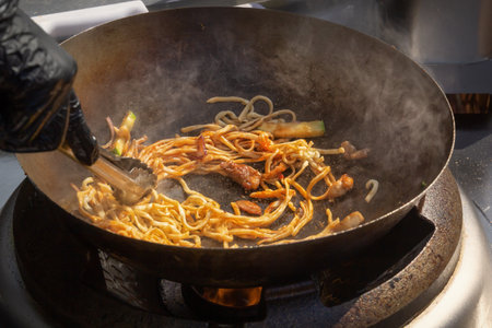 Cooking noodles with meat and vegetables in a deep wok over an open fire. street foodの写真素材