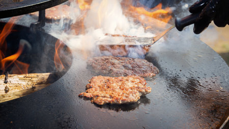 Hamburger patties are cooked in smoke on the frying plate of the grill of a street fast food restaurant.の写真素材