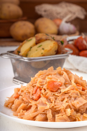 Stewed cabbage - bigos in a white porcelain plate against the background of pickled vegetables and baked potatoes. close-upの写真素材