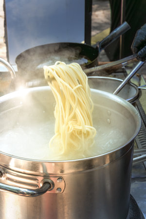 Cook takes out the boiled noodles from the pan for cooking Asian dishes in a street cafe. fast foodの写真素材