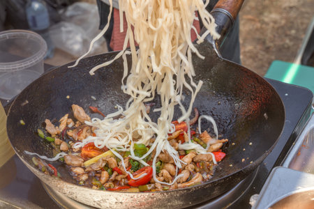 Cooking Asian noodles with meat, seafood and vegetables in a wok on the street. Fast foodの写真素材