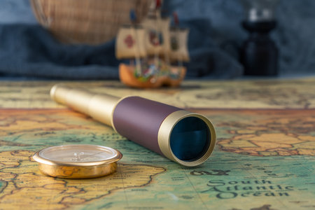Spyglass and a compass lie on an old map against the background of a model of a wooden sailboat. Close-upの写真素材
