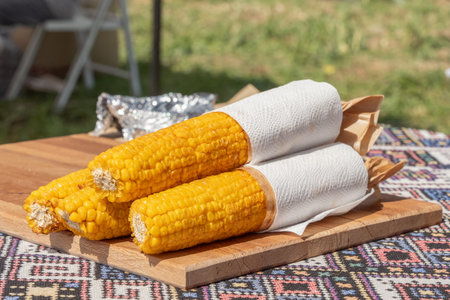 Grilled corn, sprinkled with coarse salt and red pepper, wrapped in paper napkins, prepared for...