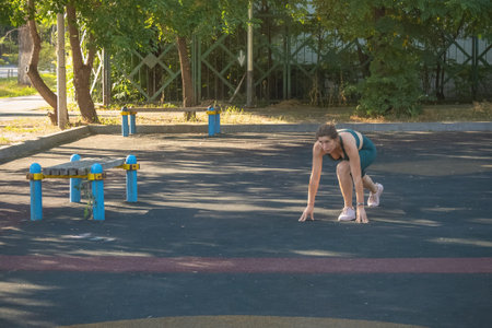 Young female athlete stands at the start and prepares to run outdoors. Healthy lifestyle