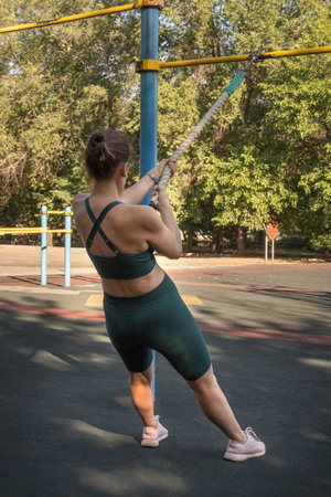 Attractive Caucasian woman doing pull-ups on a sports rope while exercising on a street sports ground. healthy lifestyleの写真素材