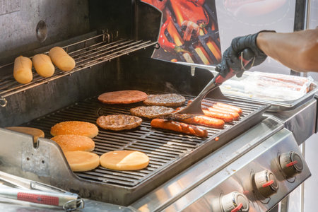 Process of cooking meat for burgers and cheeseburgers, sausages for hot dogs, buns on a grill with burning coals. street foodの写真素材
