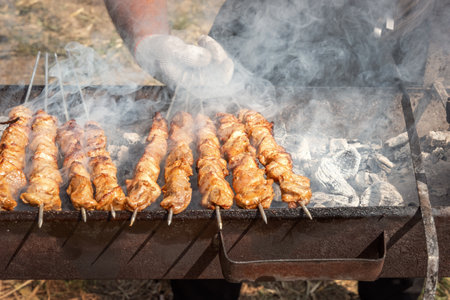 Chef's hand turns over a kebab with pieces of meat while cooking on a charcoal grill for a family party. Grill, barbecue, picnicの写真素材