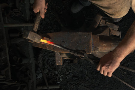 Blacksmith forges a red-hot metal piece on an anvil in a rural forge. Traditional crafts. top view