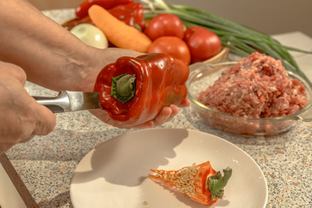 Cook uses a knife to cut out the stem with seeds from a red bell pepper for subsequent stuffing. Close-upの写真素材