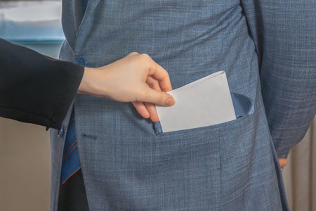 Hand puts an envelope into the pocket of a man in a suit and tie standing. Give a bribe. Corruptionの写真素材