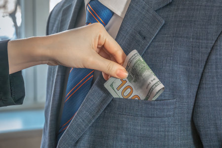 Hand puts dollar bills into the pocket of a man in a suit and tie standing opposite. To give a bribe. Corruptionの写真素材