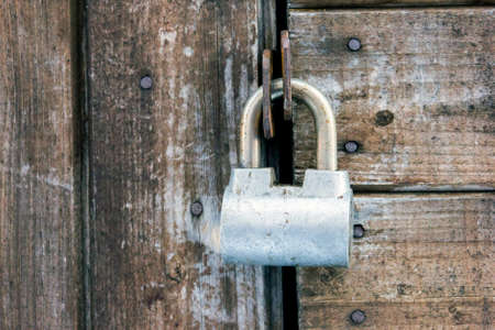 Old rusty painted metal padlock on wooden board door of shed closeupの写真素材