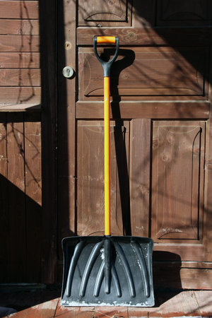 black plastic snow shovel with orange handle at the wooden door