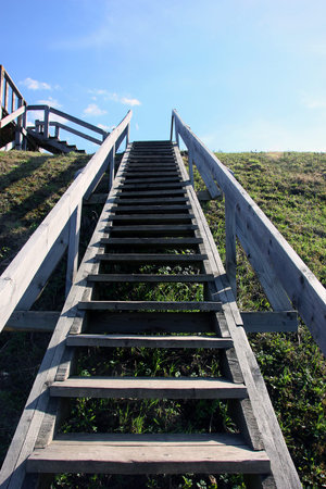 grey long wooden staircase with wooden railings on the green hill, view from the bottom up and blue...