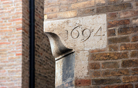 corner of old historical medieval italian red brick wall of building with date of construction on a white marble corner stone, Urbino, Italyのeditorial素材