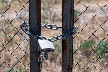 gate of wire-netting closed with padlock with thick metal chain foreground closeup