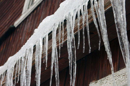 lots of white long icicles on visor of roof of wooden house in spring