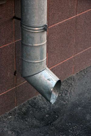 vertical metal tinplate drain pipe with bell at wall on streetの写真素材