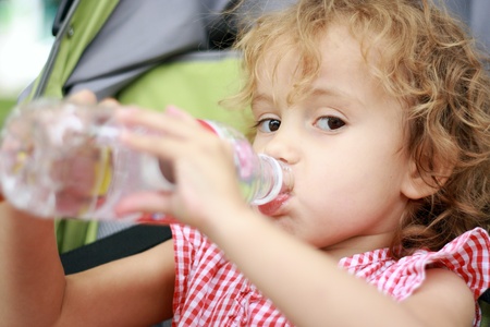 Beautiful girl seat in pram and is drinking water from plastic bottle.の写真素材