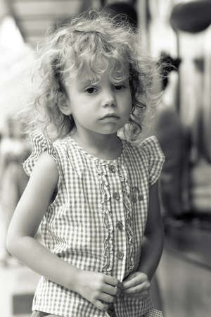Little beautiful girl sad on the street. Girl 3 years with curly hair outdoors.の写真素材
