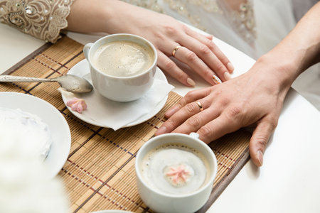 white cups of coffee on the table and hands in wedding ringsの写真素材