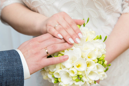 hands of newlyweds in wedding rings against the background of the wedding bouquetの写真素材