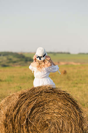 a girl in a white dress sitting on a haystackの写真素材