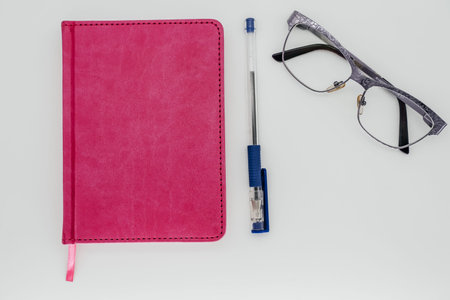 Notebook with pen and glasses on white background close-up. View from above