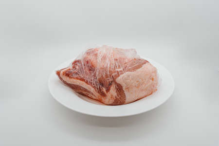 A piece of raw meat in a package on a white plate. Side viewの写真素材