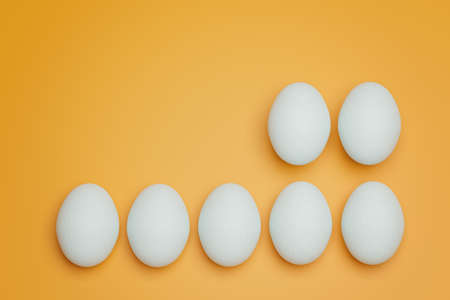 Seven white chicken eggs on yellow background top view. Creative food minimalistic background.の写真素材