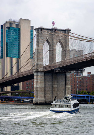 Iconic Brooklyn Bridge spanning the East River with Manhattan skyline in the background and a boat passing below. Perfect for travel, tourism, architecture, and New York City lifestyle themesの写真素材