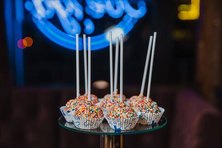 Delicious cake pops, sprinkled with colorful balls, lie on a glass stand.の写真素材