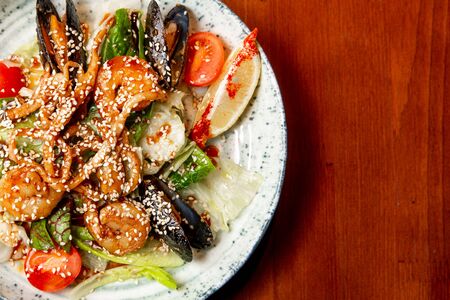Salad of fresh seafood, mussels, shrimp, fresh vegetables and greens on a wooden background.の写真素材