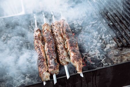 The cook is cooking kebab. The cook is cooking kebab. Four skewers with meat are prepared.の写真素材