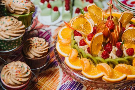  Fruit mix. Orange, mandarin, kiwi, banana, apple, strawberry and raspberry. Slices of fruit on a plate. Muffins stand next to the fruit.の写真素材