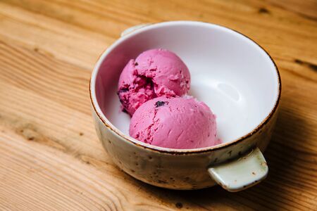 Two balls of pink ice cream in a bowl on a wooden table.の写真素材