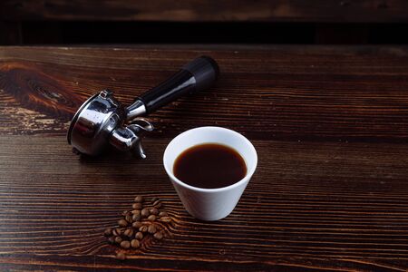 A cup of black coffee, roasted coffee beans and an espresso machine holder on a dark background.の写真素材