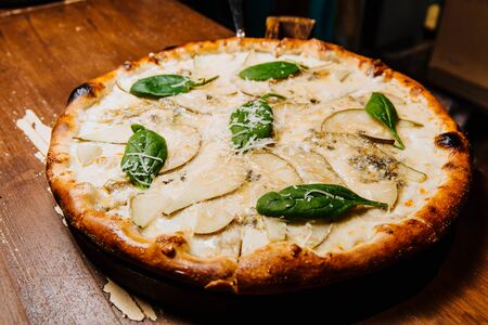 Delicious pizza with chopped pears and dor blue cheese lies on a wooden table.の写真素材