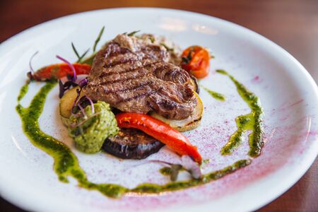 A juicy, appetizing steak with vegetables, cooked on the grill, lies on a white plate with green sauce.の写真素材