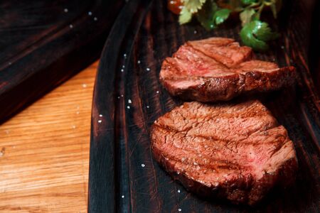 Thick juicy portions of fried fillet steak are served, sprinkled with salt, on an old wooden board. The dish is ready to serve.の写真素材