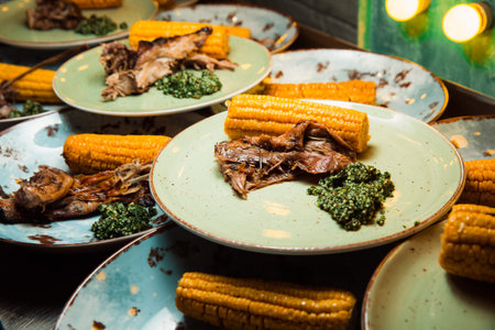 Juicy, freshly prepared meat is served on the cob of corn and green sauce. The food lies on a round plate. Ready to serve.の写真素材