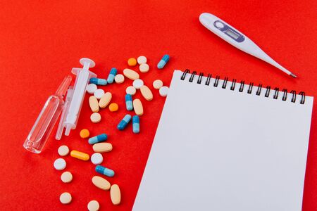 Notepad, a medicines, thermometer, syringe and ampoules on a red background.の写真素材